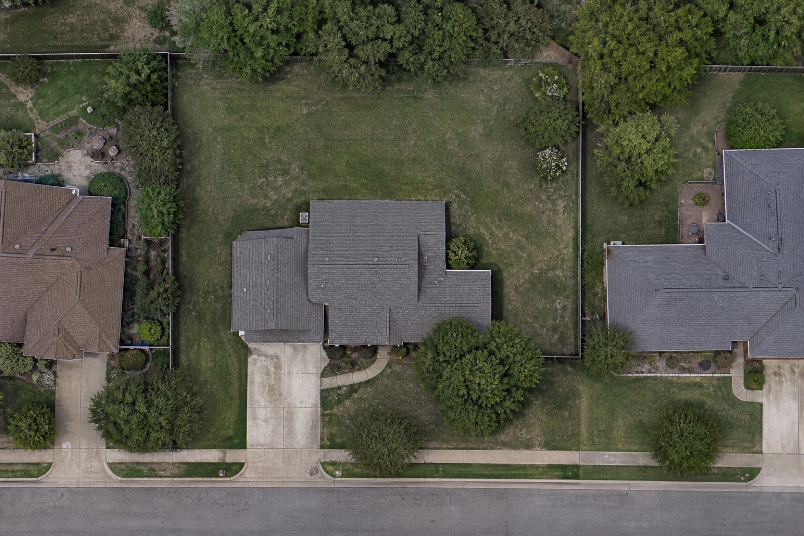 Illustrative baseline aerial view of a suburban home, yard, driveway, and neighboring parcels before hardscape work